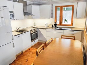 Een kleine keuken met witte kastjes, een houten eettafel en een raam met gezandstraald glas.