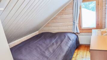 A small, single-bed room with a sloped ceiling, wooden walls, and a window with curtains.