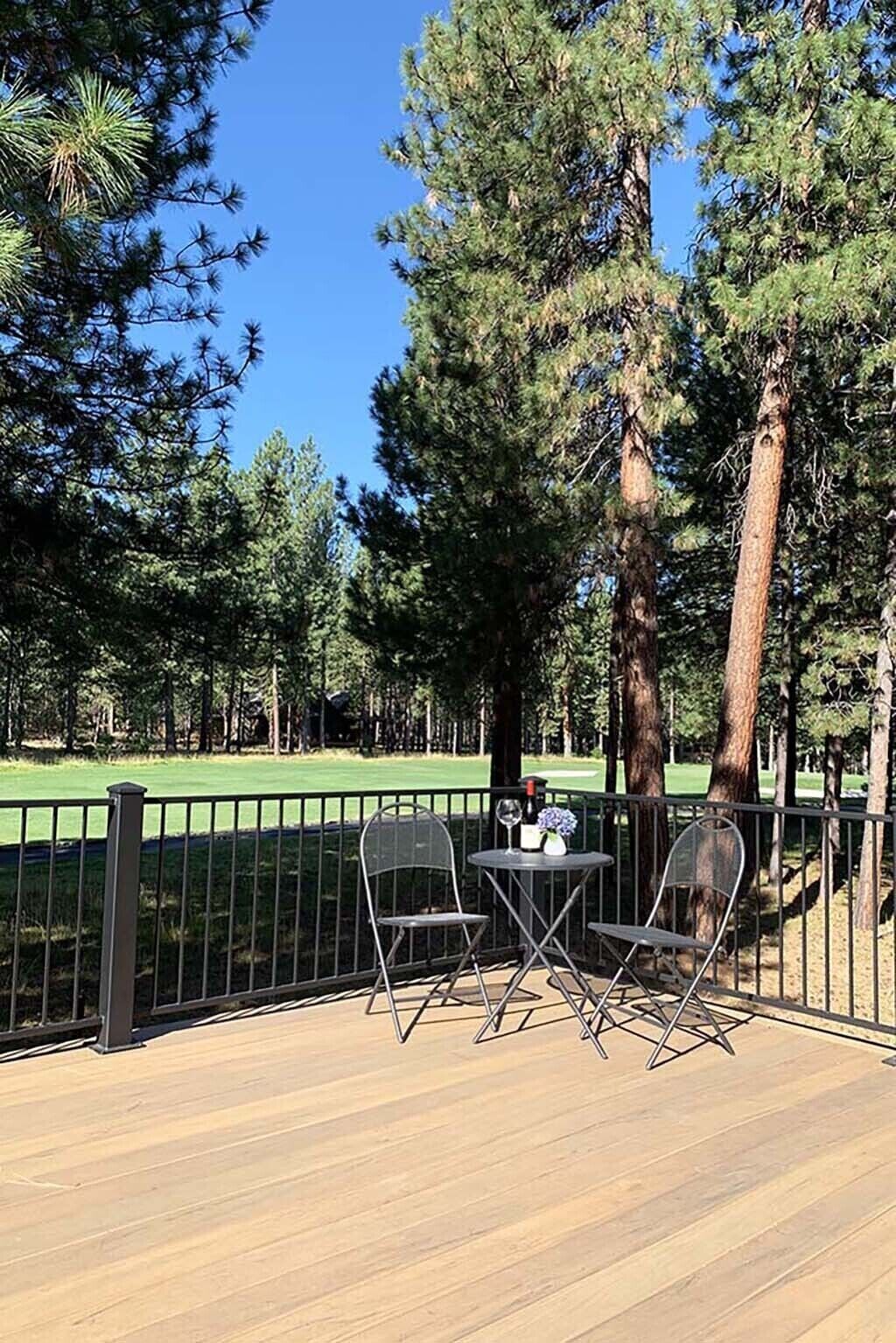 A deck with two chairs and a table, overlooking a golf course with trees.