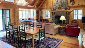 L’intérieur d’un chalet rustique, avec une cheminée en pierre, une table à manger en bois et un coin salon confortable.