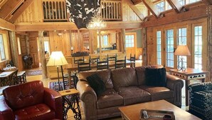L’intérieur d’un chalet rustique, avec un plafond haut, des poutres en bois, un canapé en cuir, un coin repas et une cuisine.