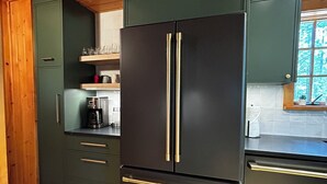 Une cuisine avec un réfrigérateur noir, des armoires en bois et une fenêtre.