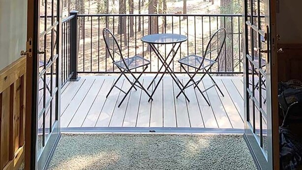 Une terrasse en bois avec une porte vitrée donnant sur une zone boisée, comprenant deux chaises et une petite table.