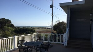 A deck with a table and chairs, a white railing, and a view of the ocean.