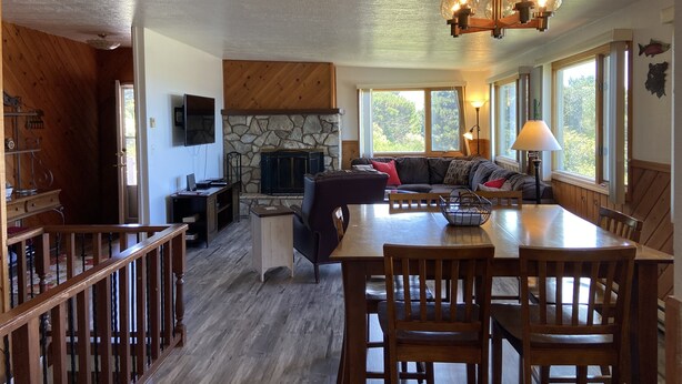 A cozy living room with a stone fireplace, a wooden ceiling, and a large window overlooking greenery.