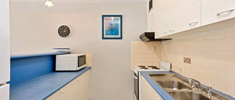 Una cocina compacta con microondas, estufa, lavabo y un reloj en la pared.
