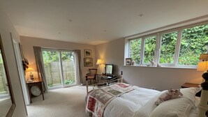 A bedroom with a large bed, a desk, a chair, and a window with a view of greenery. - Pool Lodge, rural cottage-house, self catering property, rural, North Cornwall. (Helstone)