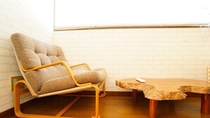 A corner room with a beige cushioned chair, a wooden coffee table, and a white brick wall. - A-Tomato Takayama Station (高山市)