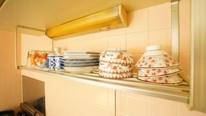 A kitchen shelf with stacked plates, a decorative bowl, and a small container. - A-Tomato Takayama Station (高山市)