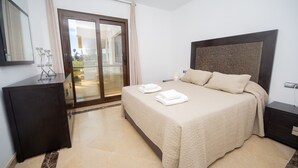 Una habitación de hotel con una cama, un aparador de madera oscura, una puerta de vidrio que da a un balcón y un espejo grande en la pared.