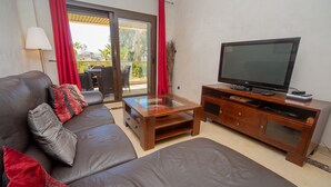 Una sala de estar con un sofá de cuero, una mesa de centro de vidrio, un mueble de entretenimiento de madera con televisor de pantalla plana y una puerta corredera de vidrio que da a un área exterior.