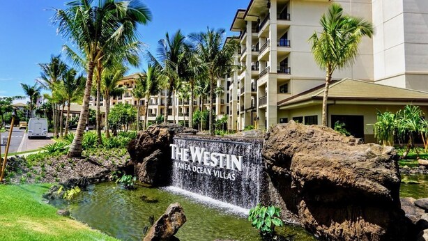 Ein Hotel Eingang mit einem Schild, auf dem 'The Westin Anaea Ocean Villas' steht, umgeben von Palmen und einem kleinen Wasserfall.