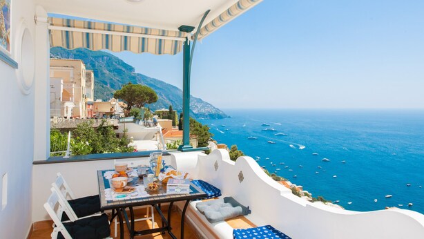 A balcony with a table set for breakfast, overlooking a coastal view with boats and mountains. - CASA PERLA - Positano AMALFI COAST (Positano)