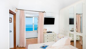 A bedroom with a bed, a dresser, a TV, and a window with curtains. - CASA PERLA - Positano AMALFI COAST (Positano)