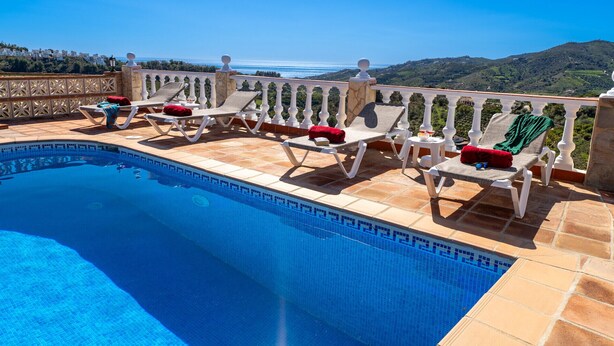 Zona junto a la piscina con sillones de descanso y vista al mar.