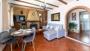 Una sala de estar con chimenea, un sofá, una mesa de comedor para cuatro comensales y un televisor montado en la pared.