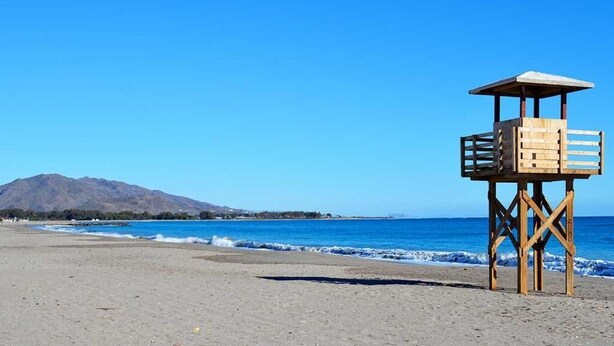 Una torre de salvavidas en una playa con cielos despejados y una montaña al fondo.