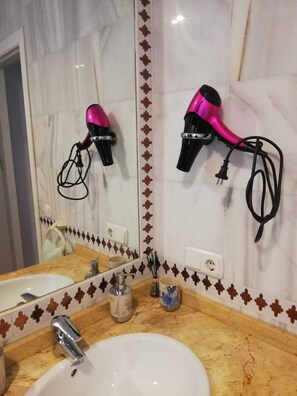 Ein Badezimmer mit Waschbecken, Spiegel und zwei an der Wand befestigten Haartrocknern.