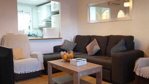 Una sala de estar con un sofá, sillones, una mesa de centro y una cocina al fondo.