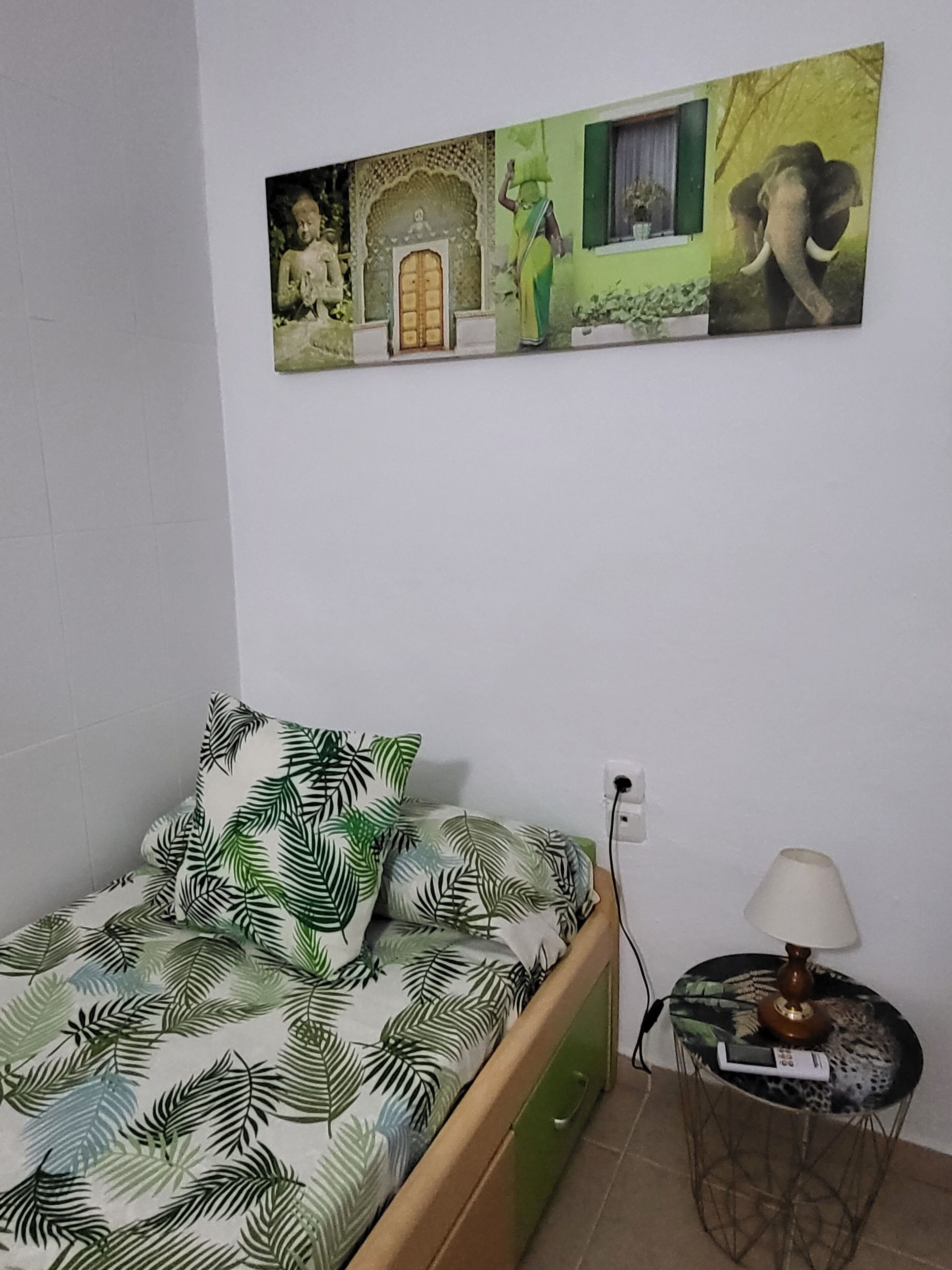 Ein Schlafzimmer mit einem Bett, einem Nachttisch, einer Lampe und einem Wandbild.