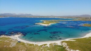 An aerial view of a coastal area with clear blue waters, sandy beaches, and distant mountains. - No 8 Leitirshask, Ballyconneely - Full Of Country Living Chic. (Ballyconneely)