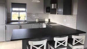 A modern kitchen with a large island, white chairs, a kettle, and a window with a view. - No 8 Leitirshask, Ballyconneely - Full Of Country Living Chic. (Ballyconneely)