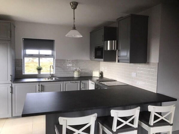 A modern kitchen with a large island, white chairs, a kettle, and a window with a view. - No 8 Leitirshask, Ballyconneely - Full Of Country Living Chic. (Ballyconneely)