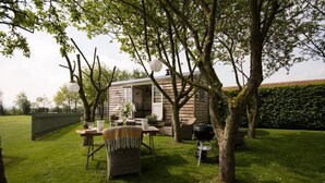 A cozy outdoor seating area with wicker furniture, a barbecue grill, and a small wooden structure. - Secluded and Luxurious Shepherd's Hut (Melksham)