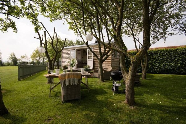 Un área de estar al aire libre acogedora, con mobiliario de mimbre, una parrilla y una pequeña construcción de madera.