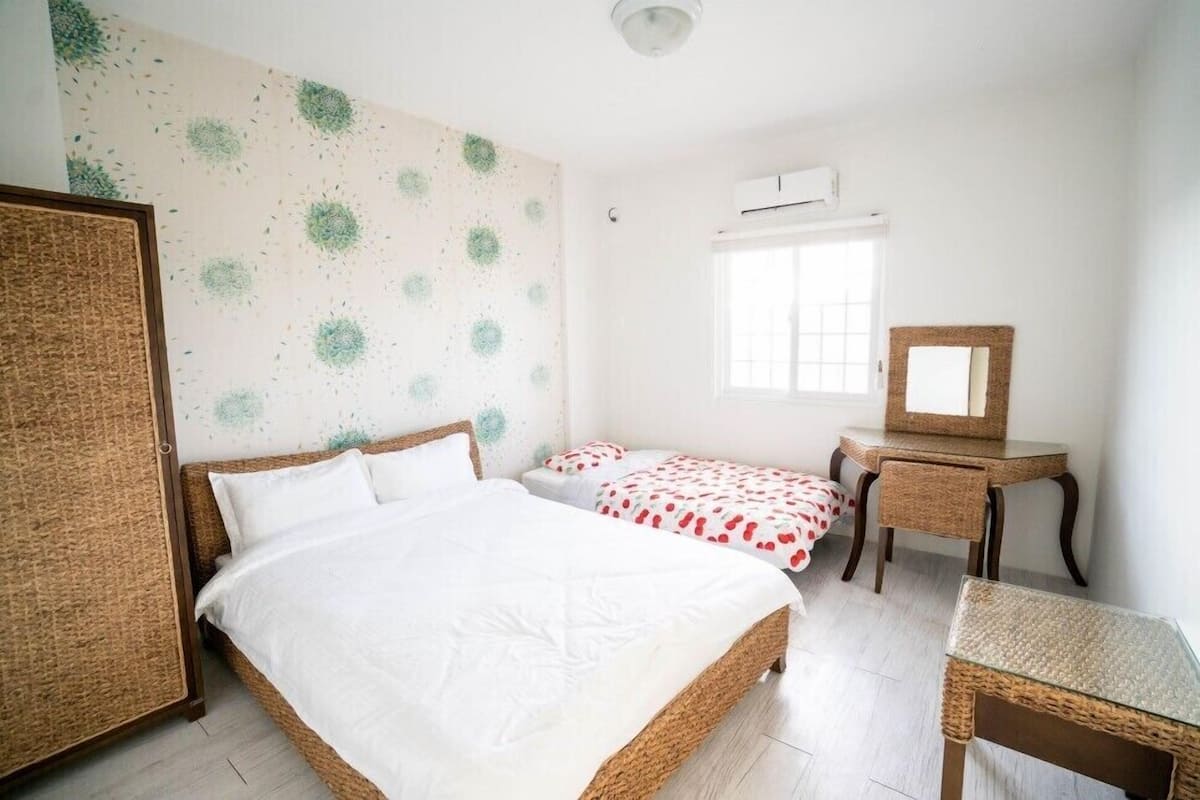 A bedroom with a large bed, two smaller beds, a desk, and a mirror.