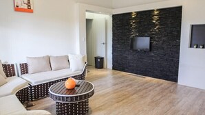 A modern living room with a sectional sofa, a round coffee table, and a flat-screen TV mounted on a stone wall. - Karis Villa (Saipan)