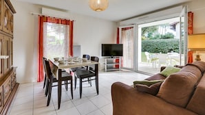 Een woonkamer met een bank, televisie, eettafel, stoelen en uitzicht door een glazen deur op een buitenruimte.