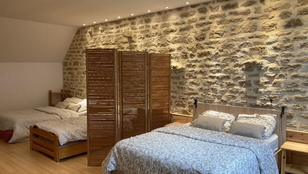 Un dormitorio con pared de piedra, dos camas, un armario de madera y una mesita de noche.