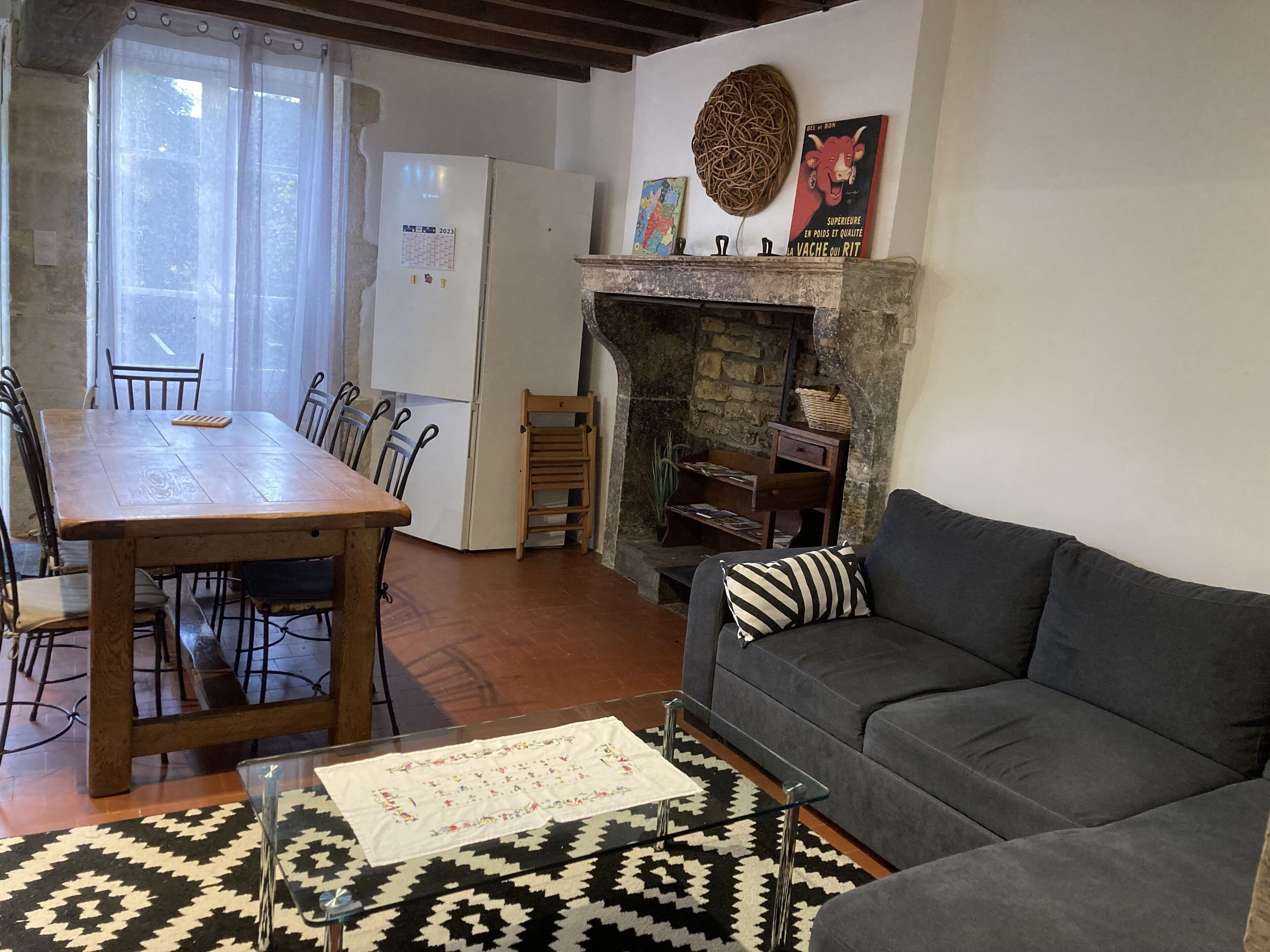 Una sala de estar con sofá, una mesa de comedor con sillas, chimenea y refrigerador.