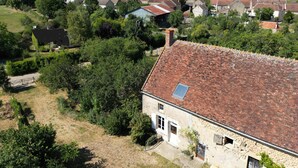 Un edificio de piedra con techo de tejas, rodeado de vegetación y otras edificaciones en un entorno rural.