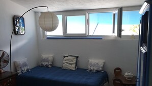A bedroom with a bed, a desk, a chair, a fan, and a window with a view. - Au Vieil, Small fisherman's house (Noirmoutier-en-l'Île)