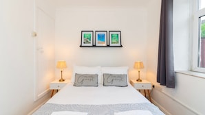 Ein Hotelzimmer mit Bett, zwei Nachttischlampen, einem Fenster mit Vorhängen und drei gerahmten Bildern an der Wand.