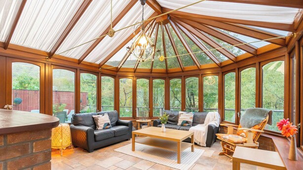 Ein Wintergarten mit Holzboden, großen Fenstern, einem Kamin und einer Sitzecke mit einer Couch und Sesseln.