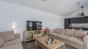 A modern living room with a sofa, a coffee table, a TV, and a kitchen area with cabinets and a countertop. - Luxury villa Sorella in Istria, private pool (Barban)