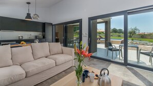 A modern living room with a sofa, a dining area with chairs, a kitchen, and a large sliding glass door leading to an outdoor patio. - Luxury villa Sorella in Istria, private pool (Barban)