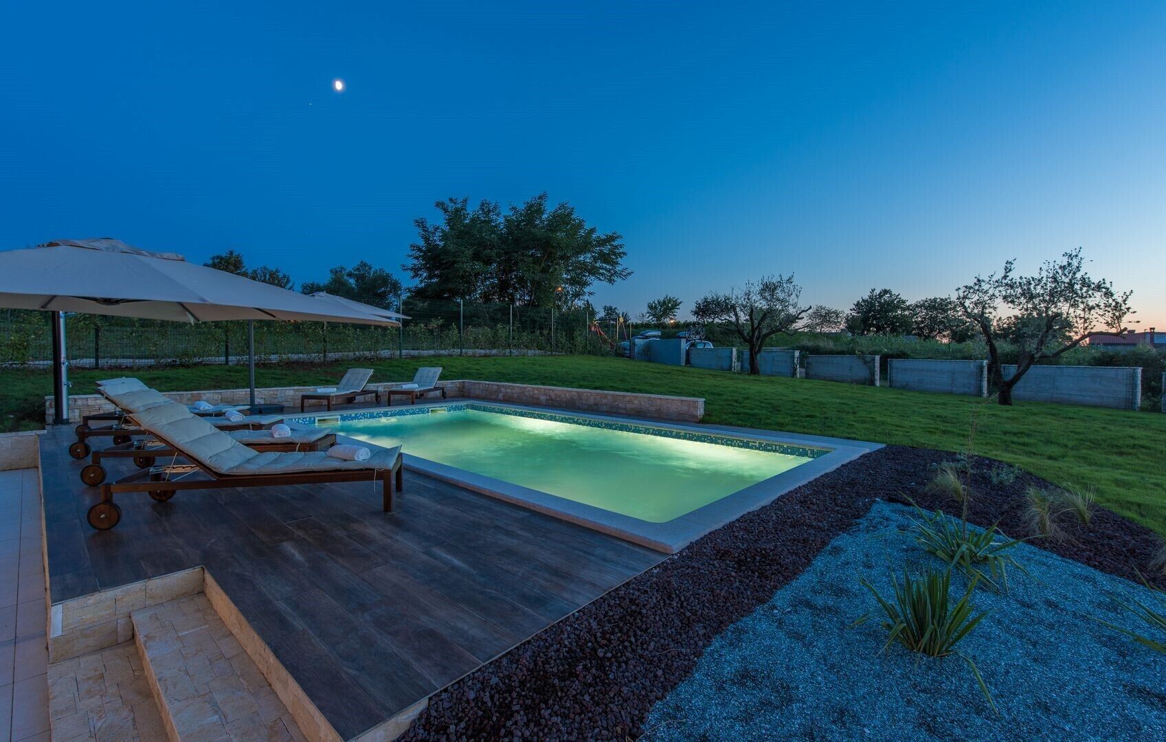 Une piscine rectangulaire dont le bord est recouvert de carrelage, entourée d’une terrasse en bois et de chaises longues.