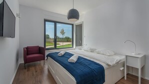 A modern bedroom with a large bed, a red chair, a bedside table with a lamp, and a view of the outdoors through a large window. - Luxury villa Sorella in Istria, private pool (Barban)