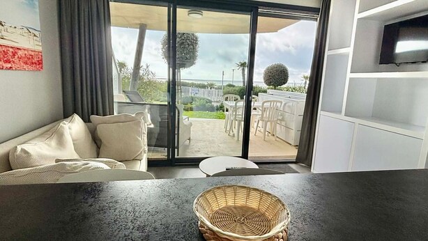 Un salon moderne avec un canapé, une table et une grande porte-fenêtre coulissante donnant sur une terrasse extérieure.