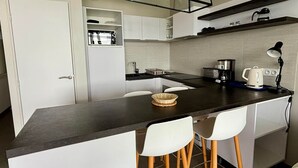 Une cuisine moderne dotée d’un îlot central, de meubles blancs, d’un four encastré et d’une machine à café.