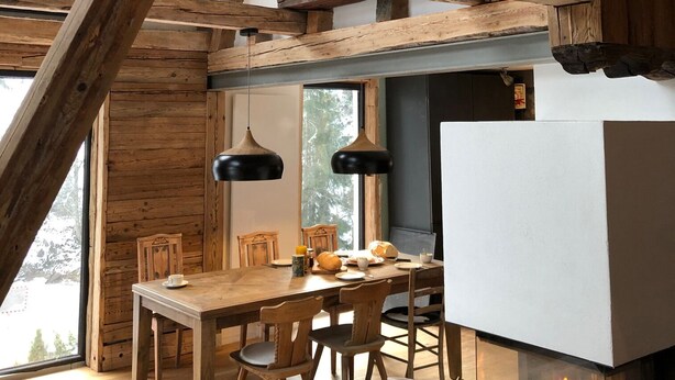 A rustic interior with exposed wooden beams, a dining area with wooden chairs and a table, and a fireplace with visible fire. - Schönbacher Hof with a view of the Hohe Salve (Hopfgarten im Brixental)