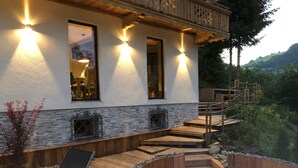 A modern building with a stone facade, wooden deck, and outdoor seating area. - Schönbacher Hof with a view of the Hohe Salve (Hopfgarten im Brixental)