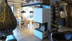 A spacious living area with a high ceiling, wooden beams, a fireplace, and hanging pendant lights. - Schönbacher Hof with a view of the Hohe Salve (Hopfgarten im Brixental)