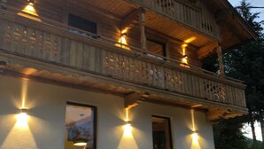 A two-story wooden building with balconies, large windows, and a stone base. - Schönbacher Hof with a view of the Hohe Salve (Hopfgarten im Brixental)