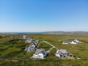 A rural village with white houses, a clear sky, and a distant view of the sea.