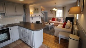 Una cocina con armarios blancos y encimera de granito, un comedor con mesa y sillas blancas, y una sala de estar con sofá y televisor.